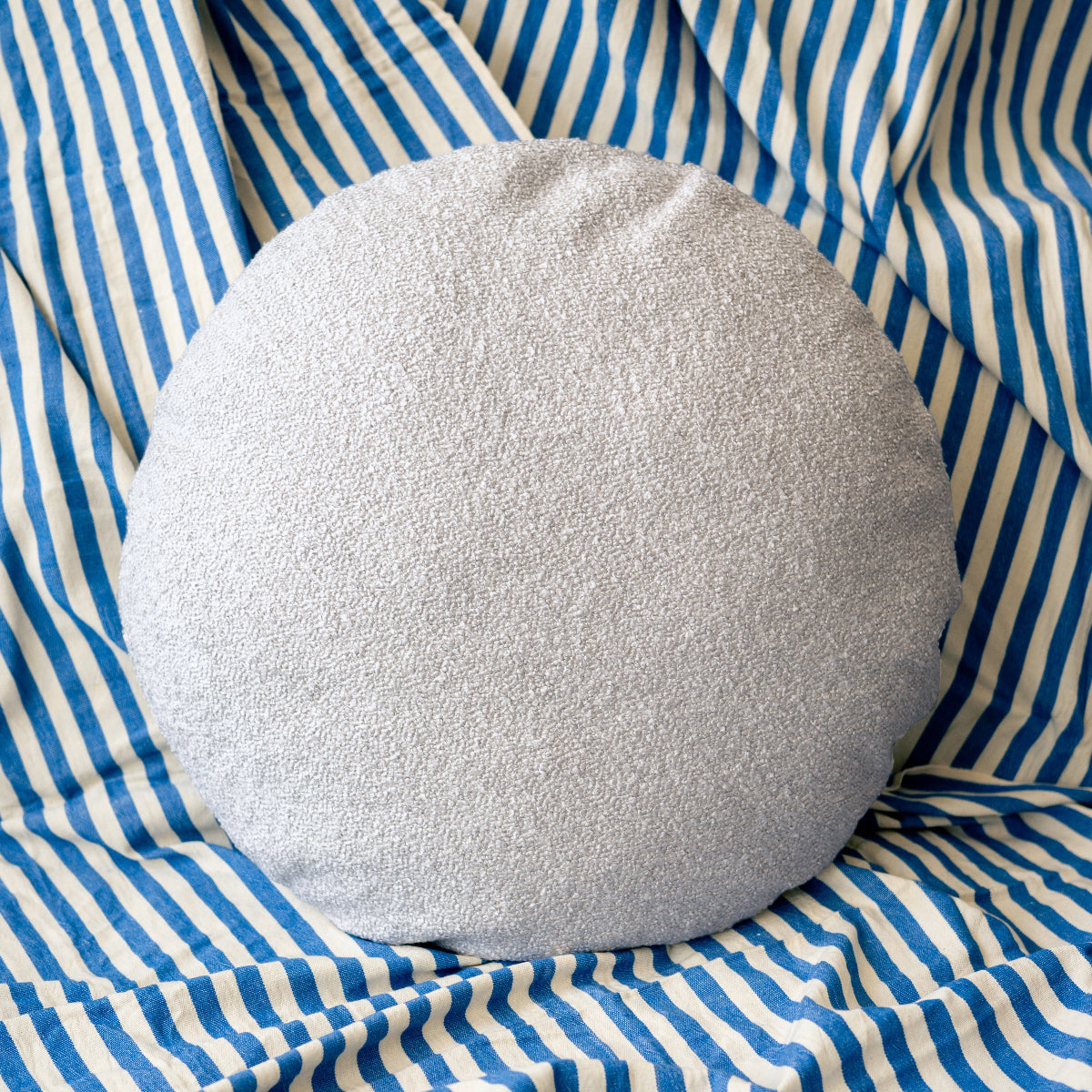Round light grey cushion on a blue and white striped fabric background