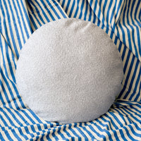 Round light grey cushion on a blue and white striped fabric background