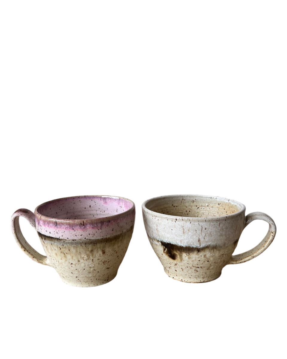 Two ceramic mugs with light and dark neutral and pink glaze details on a white background