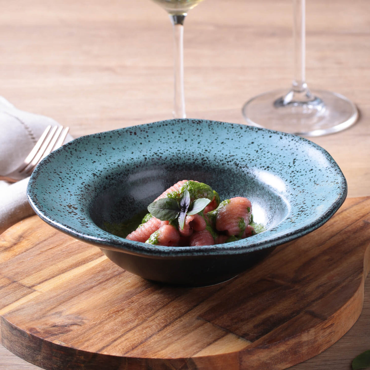 Blue ceramic bowl with a dish on a wooden table with wine glasses in the background
