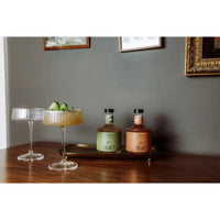 Two bottles of non-alcoholic cocktail bottles on a tray with two cocktail glasses on a wooden surface.