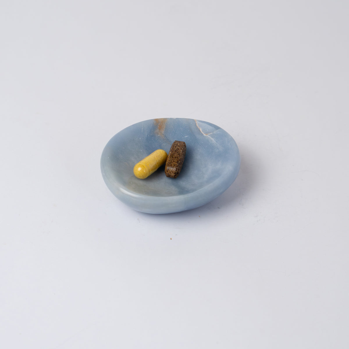 Light blue stone dish holding two pills on a white background