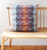 Plaid pillow on a wooden bench against a white wall