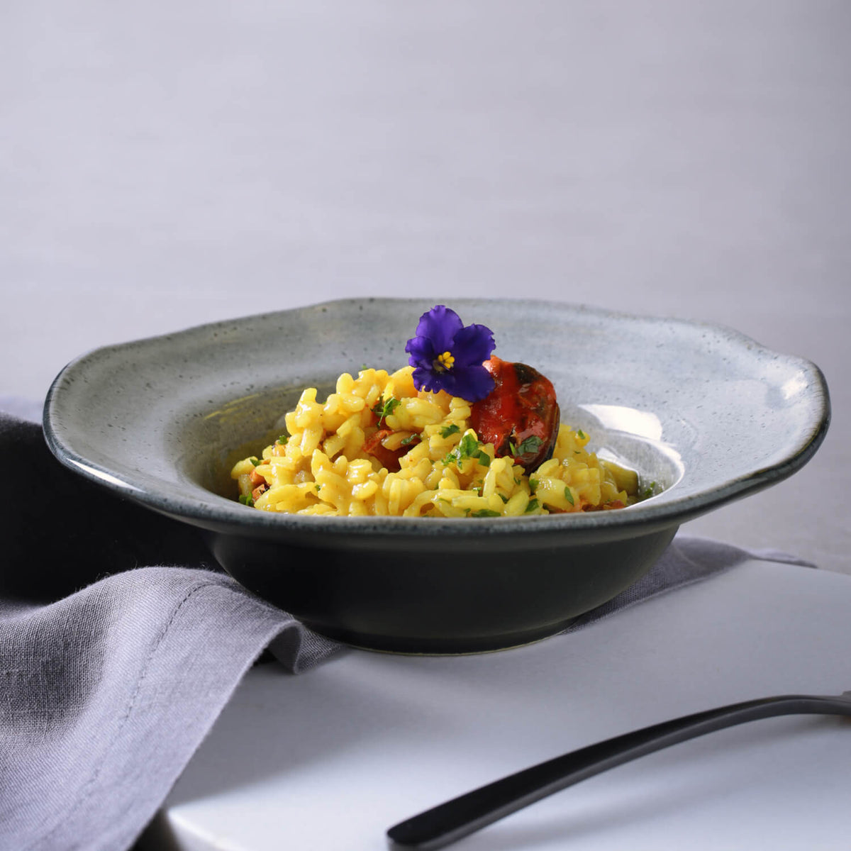 Bowl of yellow pasta with a garnish on a gray surface
