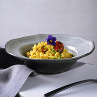 Bowl of yellow pasta with a garnish on a gray surface