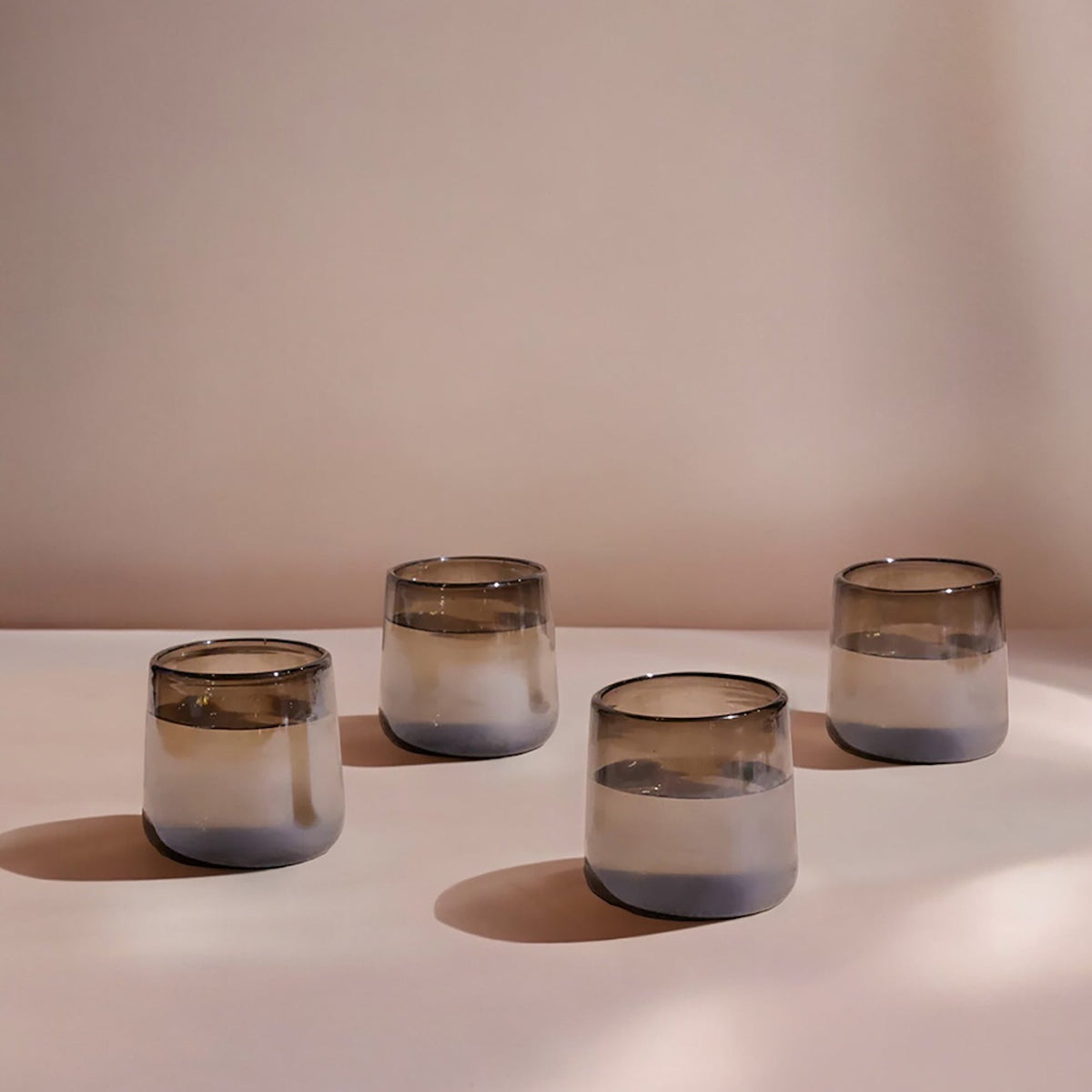 Four smoked gradient drinking glasses on a white surface with a soft pink background