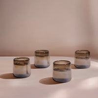 Four smoked gradient drinking glasses on a white surface with a soft pink background