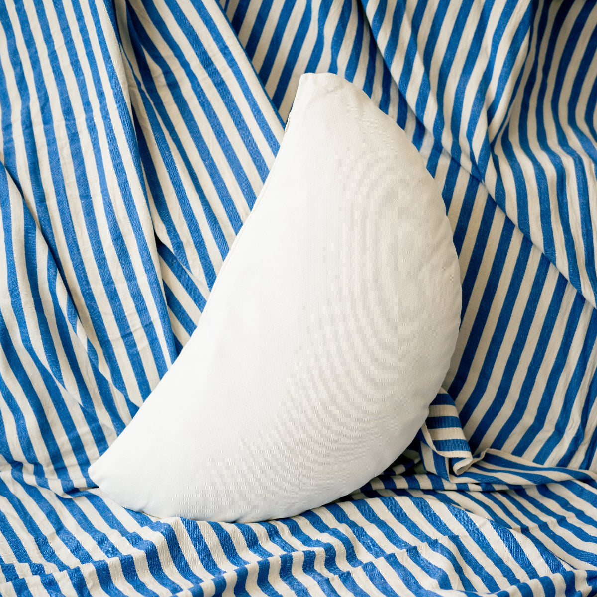 White half circle pillow on a blue and white striped fabric background