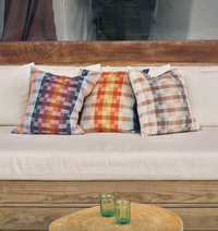 Colorful plaid cushions on a white sofa with a wooden table and glasses in the foreground.