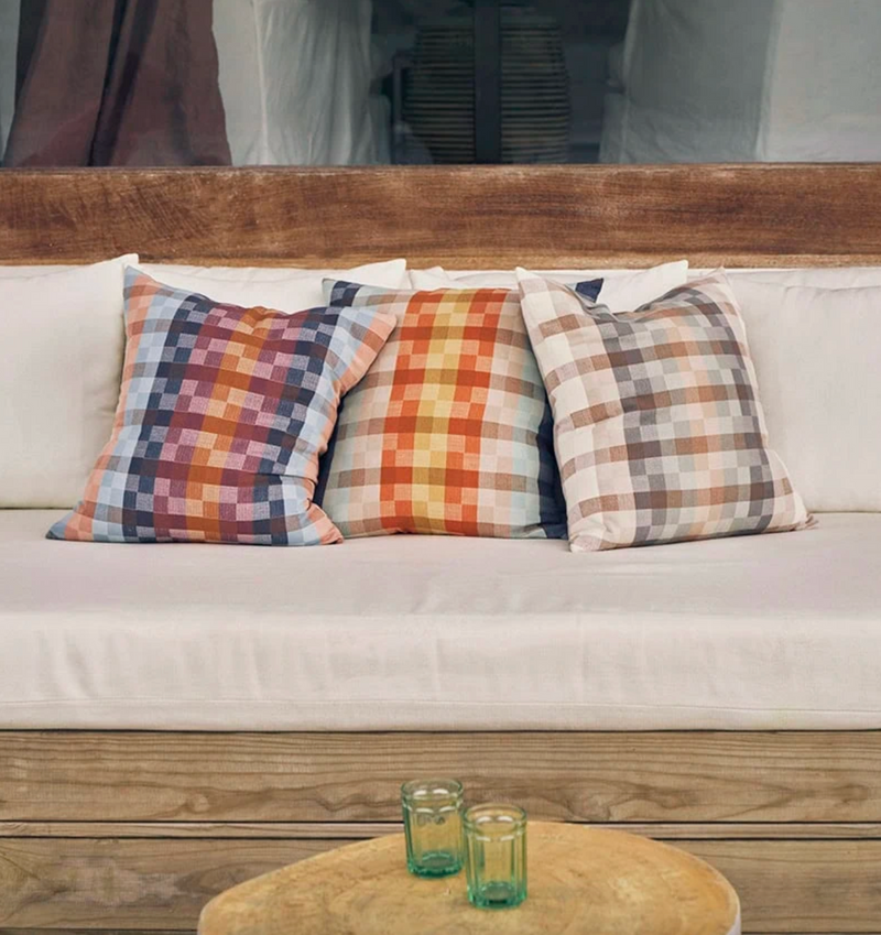 Colorful plaid cushions on a white sofa with a wooden table and glasses in the foreground.