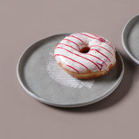 Donut with red drizzle on a gray plate against a beige background