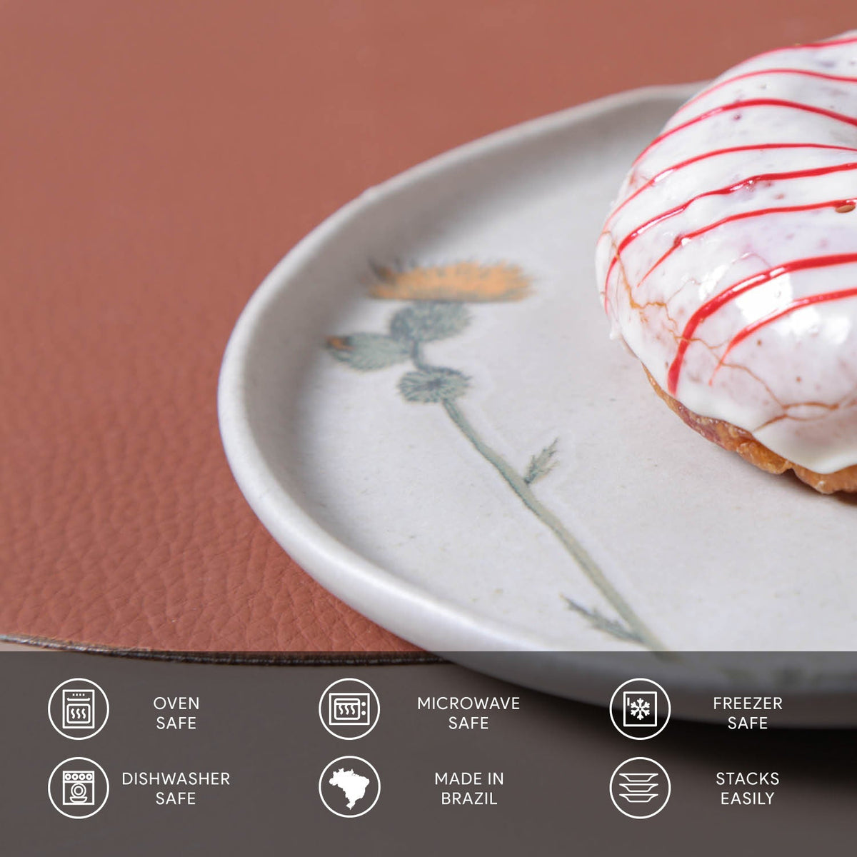 Donut with white icing and red drizzle on a ceramic plate with floral design, against a brown background.