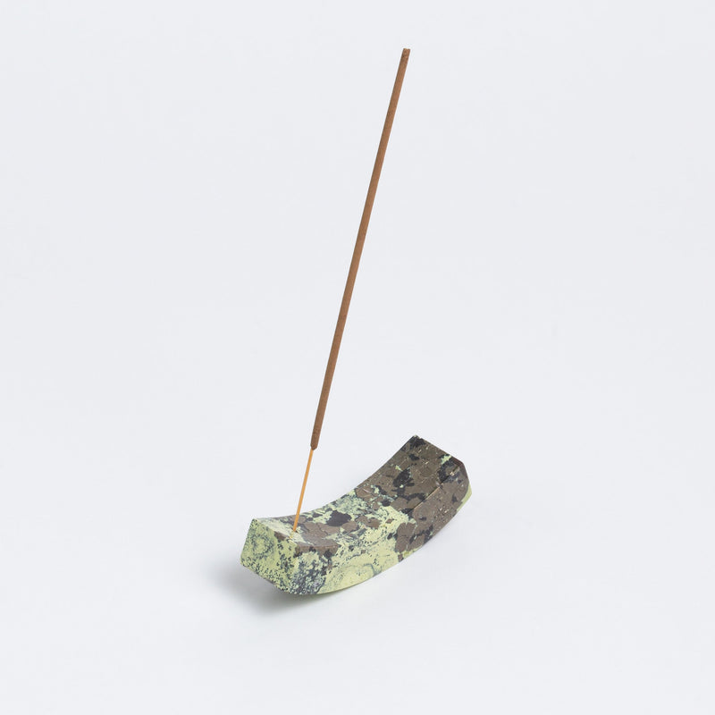Incense stick on a decorative green stone holder against a light gray background