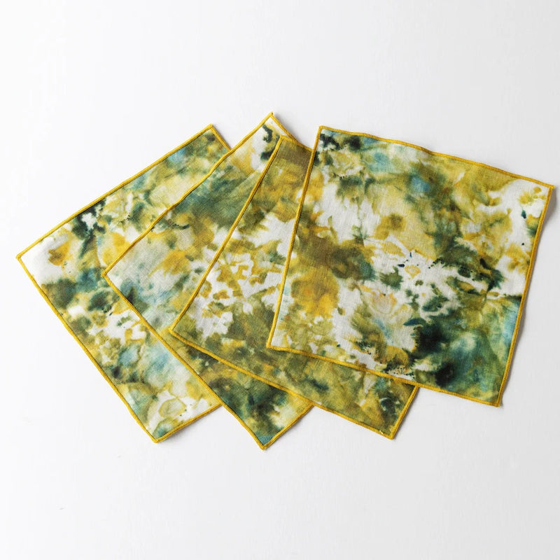 Four square cocktail napkins with a green and yellow marble pattern on a white background