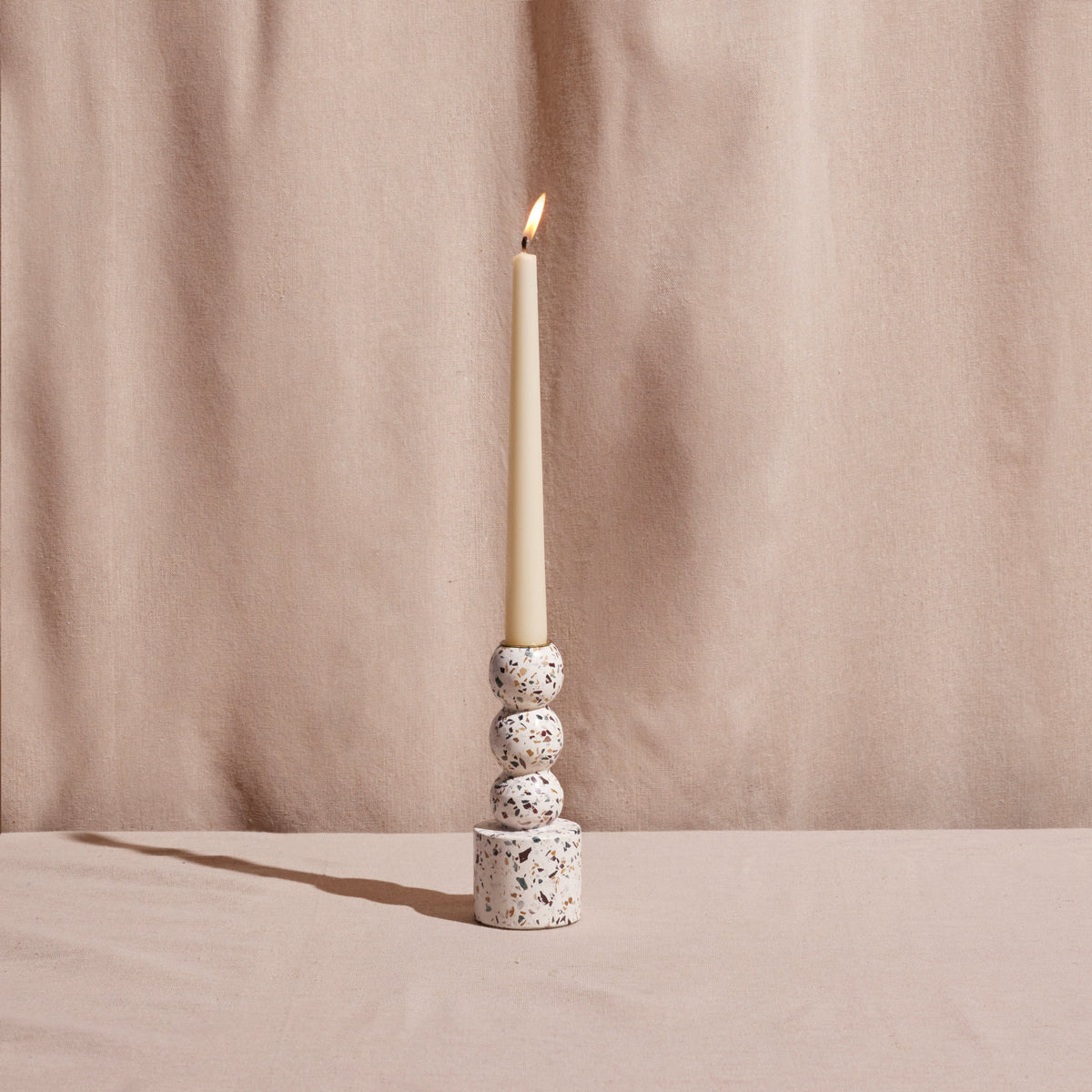 Candle in a terrazzo-patterned candle holder against a beige curtain background