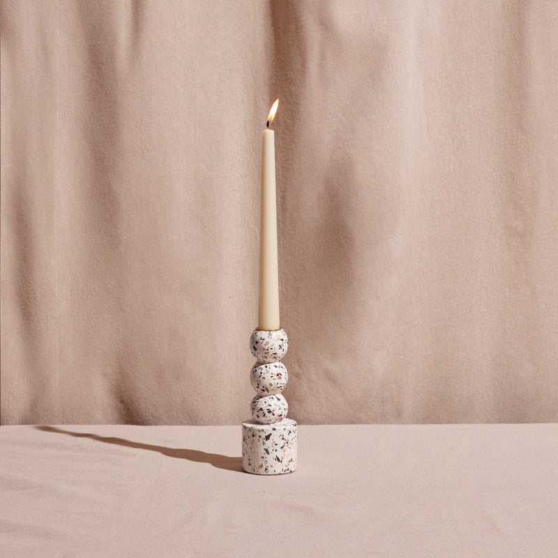 Candle in a terrazzo-patterned candle holder against a beige curtain background