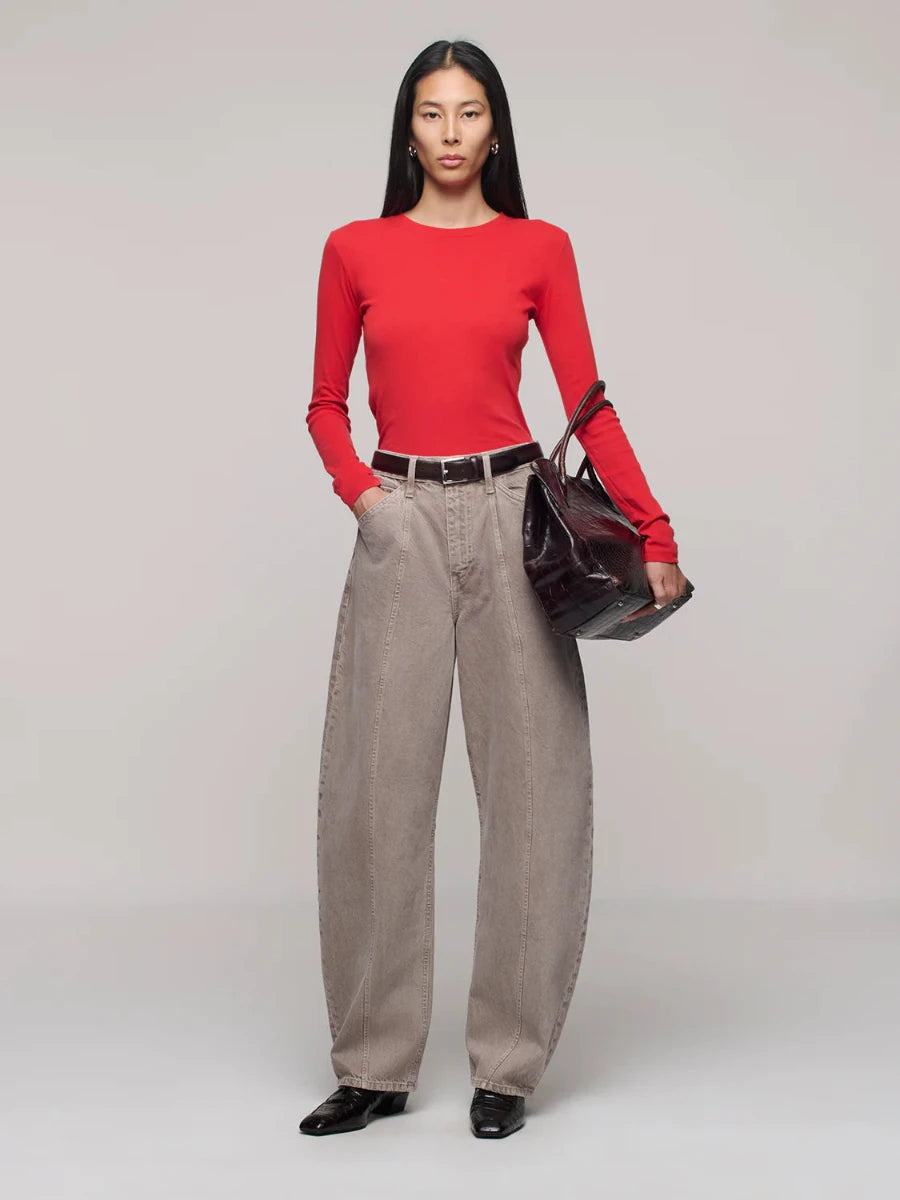 Person wearing a red top and beige pants holding a dark handbag on a plain background