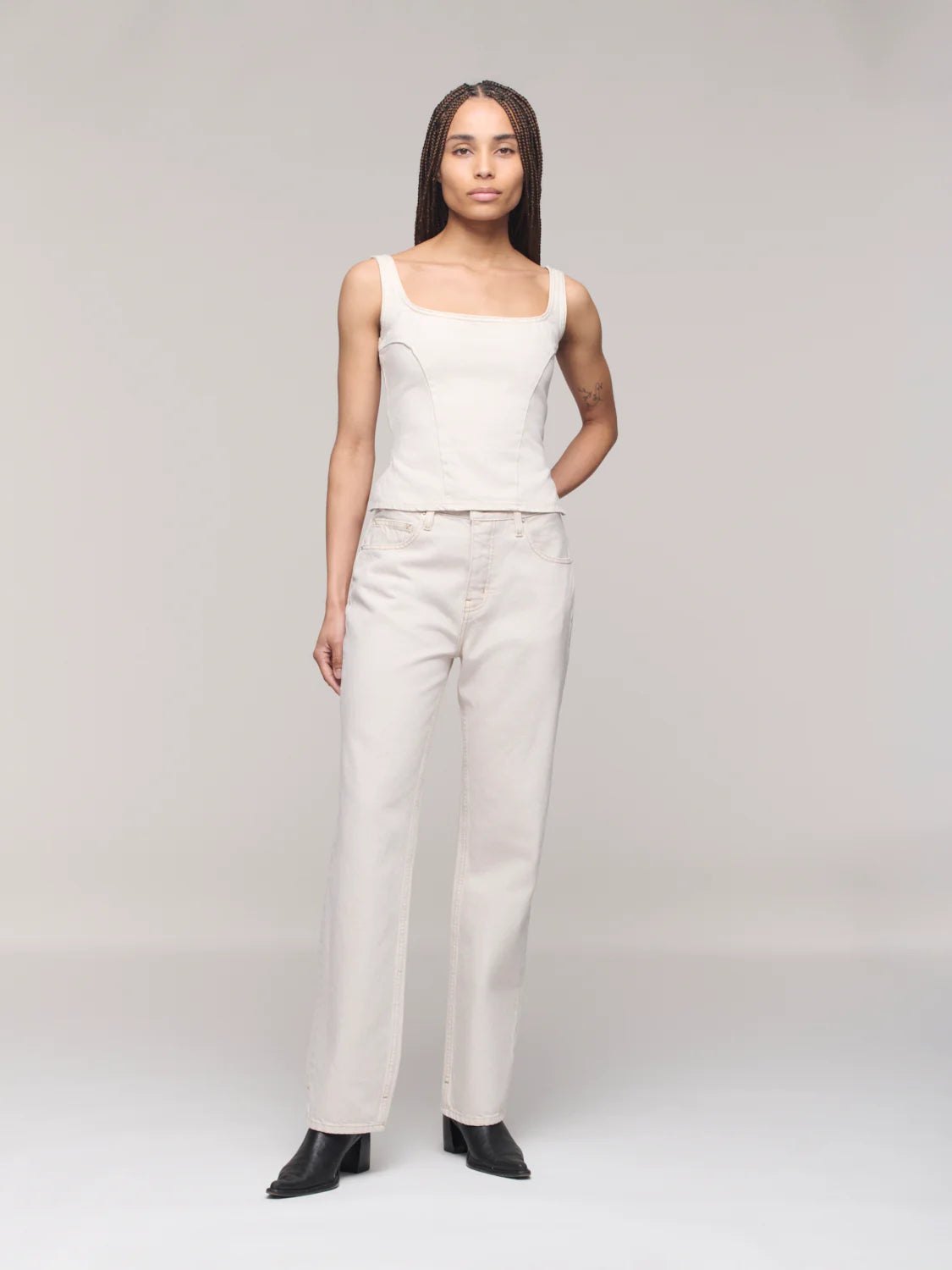 Woman wearing a white sleeveless top and pants on a plain background