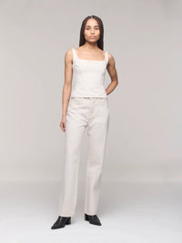 Woman wearing a white sleeveless top and pants on a plain background