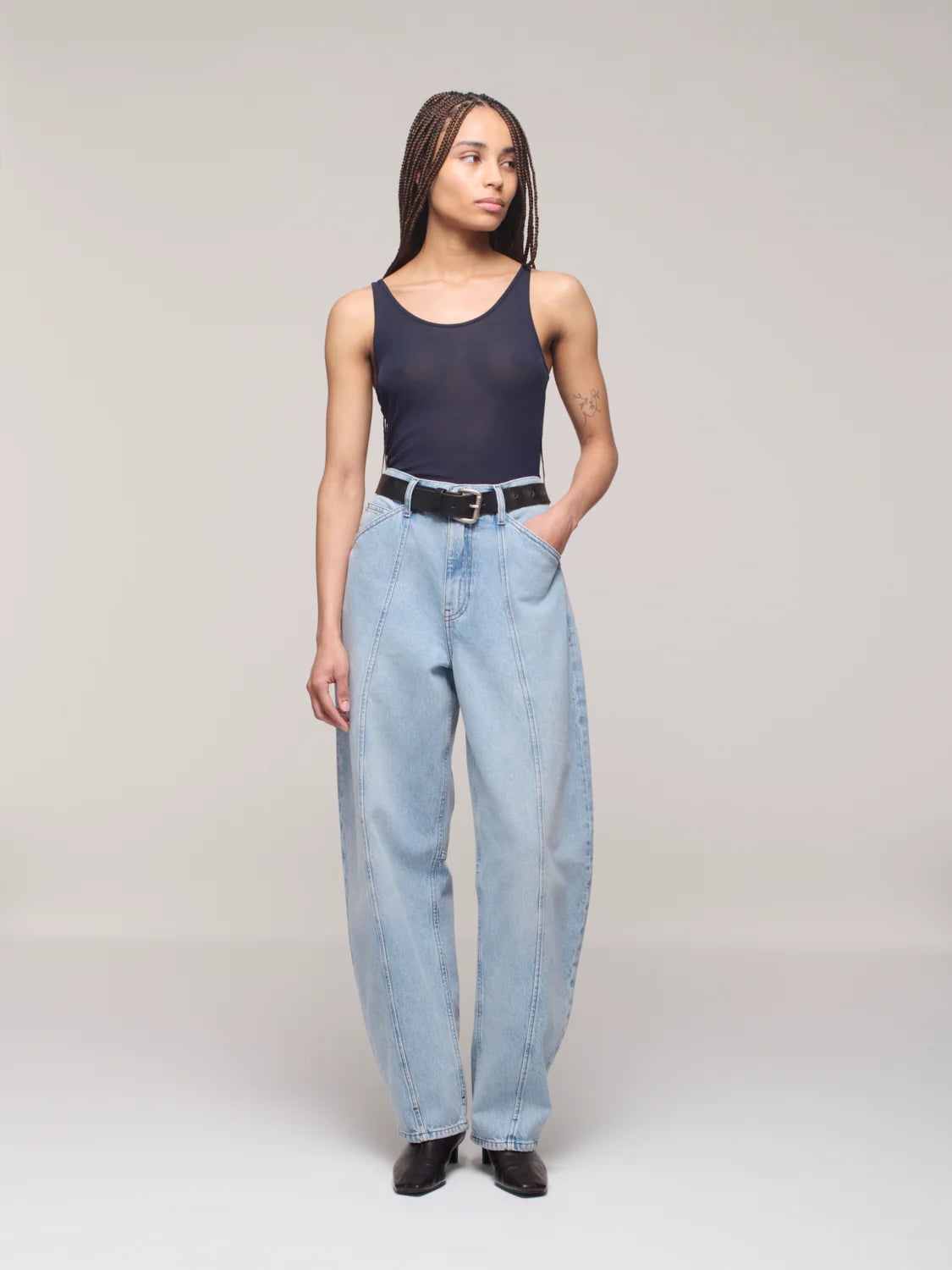 Person wearing a black tank top and light blue jeans on a plain background