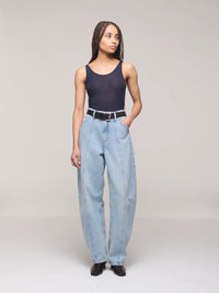 Person wearing a black tank top and light blue jeans on a plain background