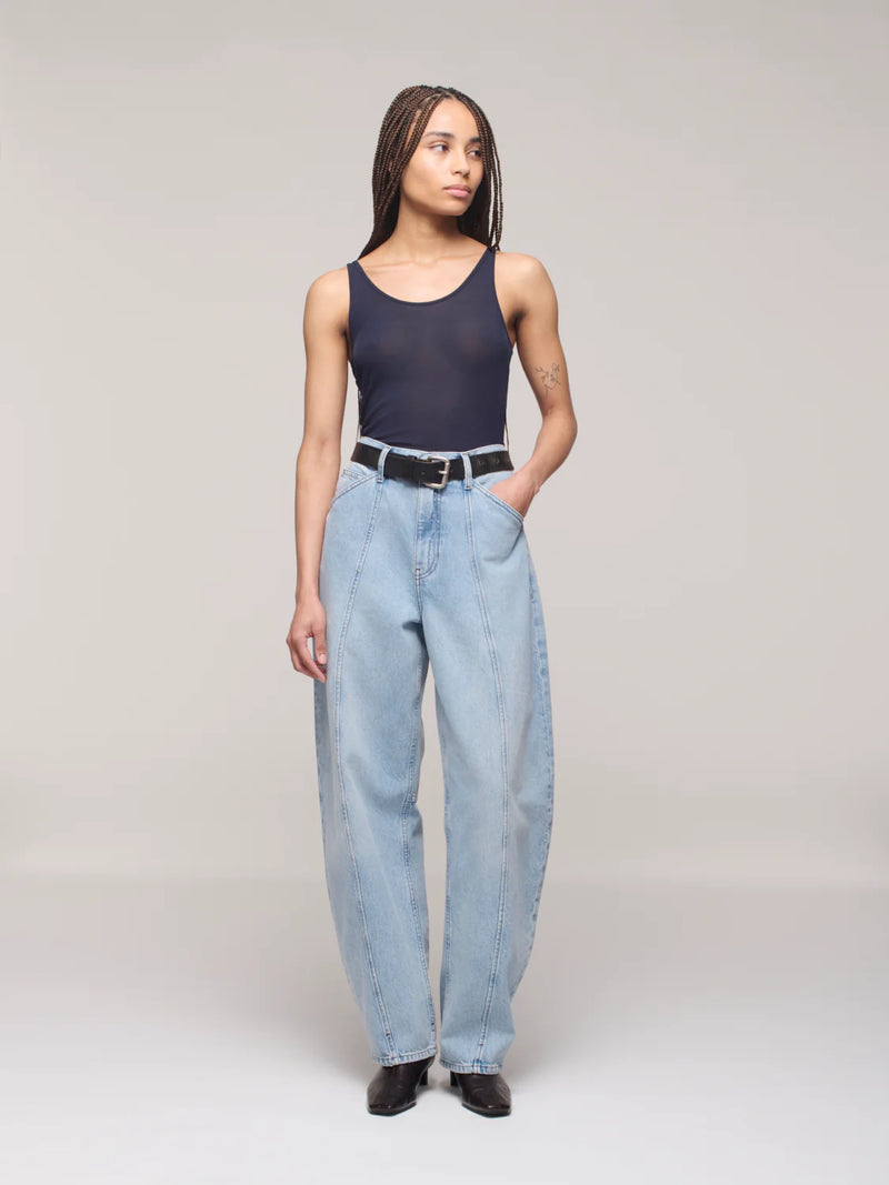 Person wearing a black tank top and light blue jeans on a plain background