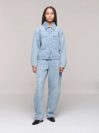 Person wearing a light blue denim jacket and jeans on a plain background 