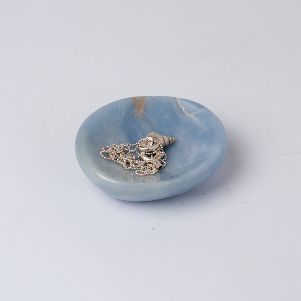 Light blue stone dish holding a silver necklace on a white bckground