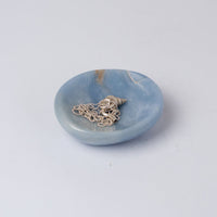 Light blue stone dish holding a silver necklace on a white bckground