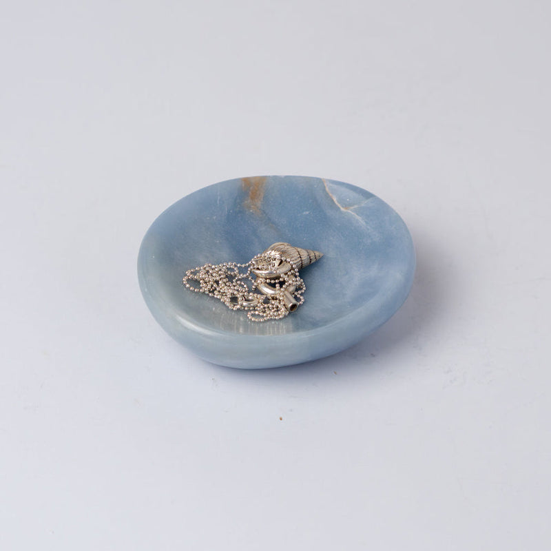 Light blue stone dish holding a silver necklace on a white bckground