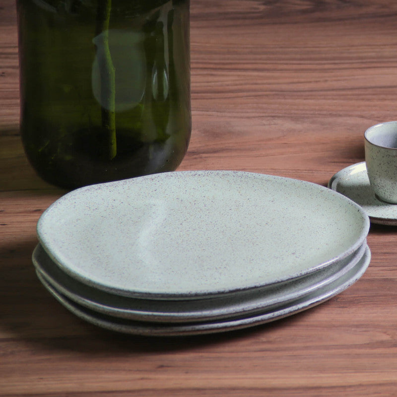 Stack of speckled ceramic plates on a wooden surface with a blurred green bottle in the background.