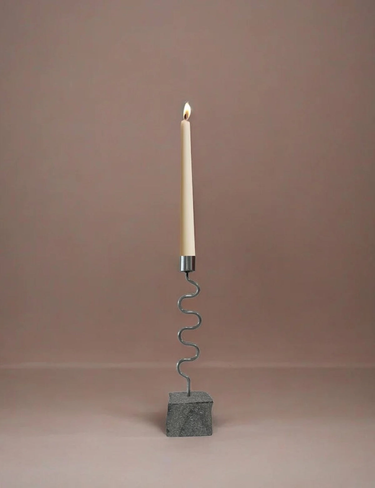 Candle holder with a wavy design and stone base, with candle on a plain background