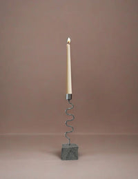 Candle holder with a wavy design and stone base, with candle on a plain background
