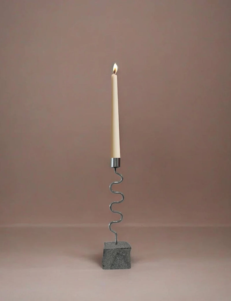 Candle holder with a wavy design and stone base, with candle on a plain background