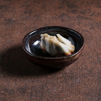 Delicate dish in a small black ceramic ramekin on a textured brown surface