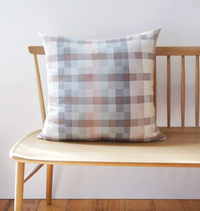 Plaid pillow on a wooden bench against a white wall
