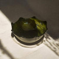 Green glass bowl on a textured surface with shadows