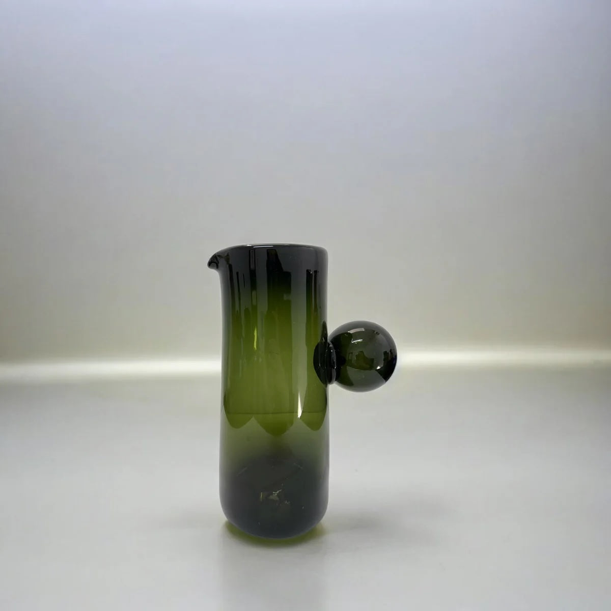 Green glass pitcher vase with a spherical accent handle on a white background
