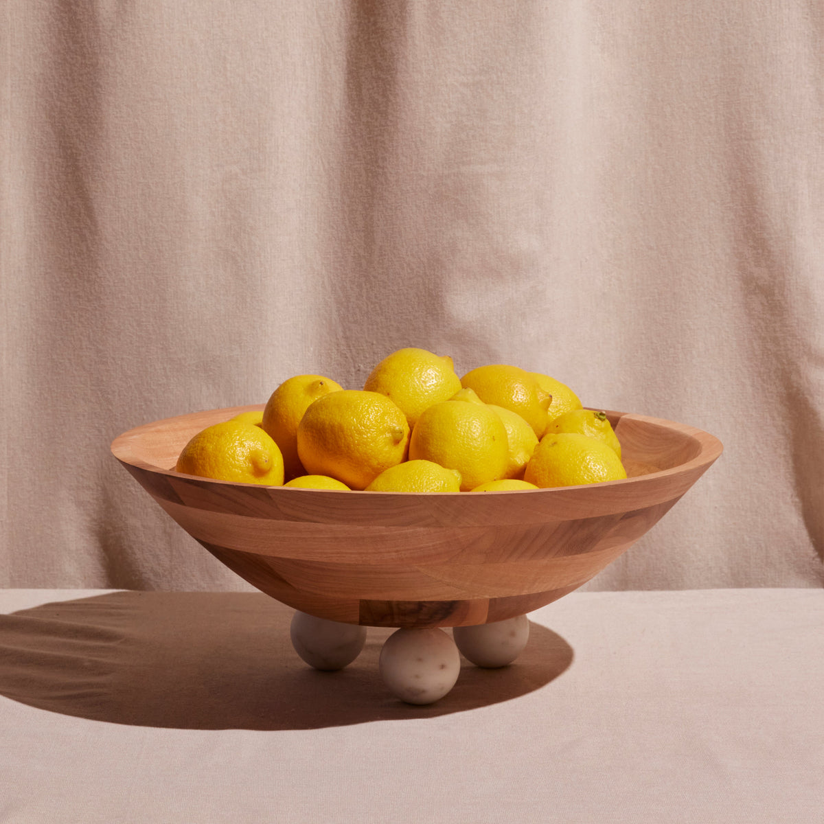 Wooden bowl filled with lemons on a beige background