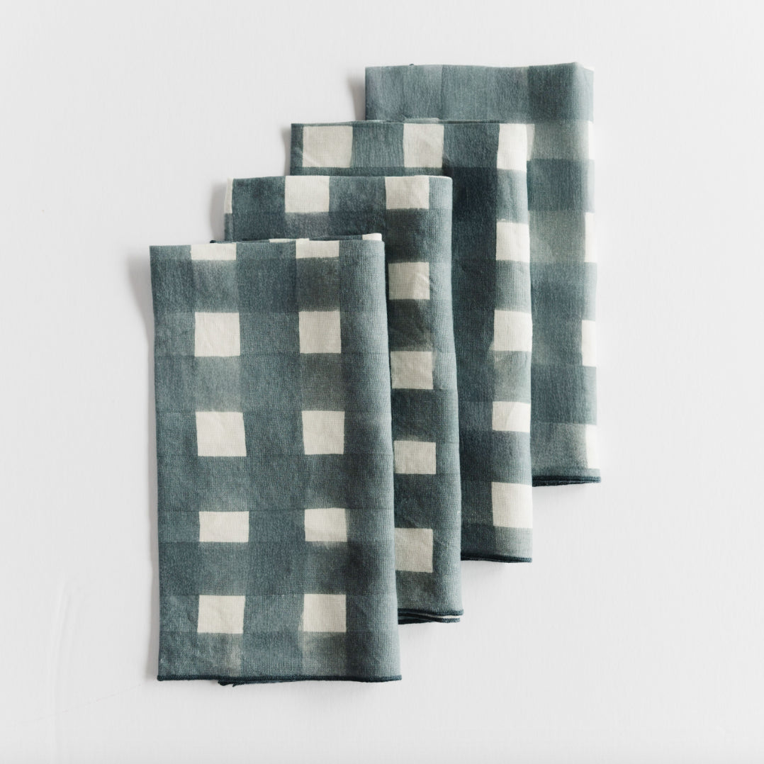 Set of four blue-grey and white checkered napkins on a light gray background