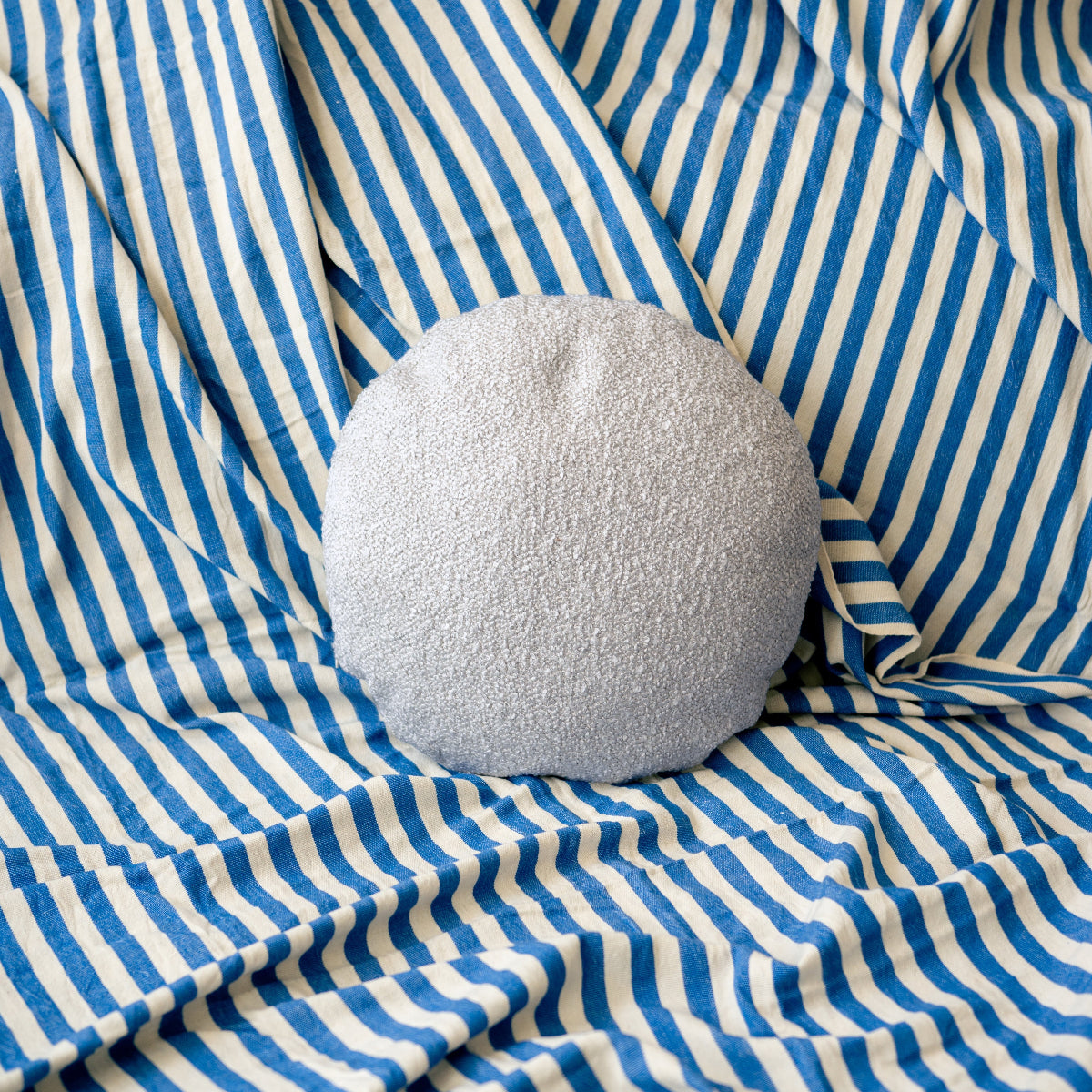Light grey textured round pillow on blue and white striped fabric
