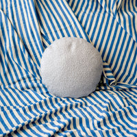 Light grey textured round pillow on blue and white striped fabric