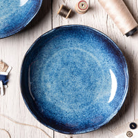 Blue ceramic plate on a wooden surface with spools of thread and buttons nearby
