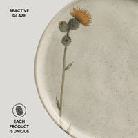 Ceramic plate with a thistle design and 'Reactive Glaze' text on a light background