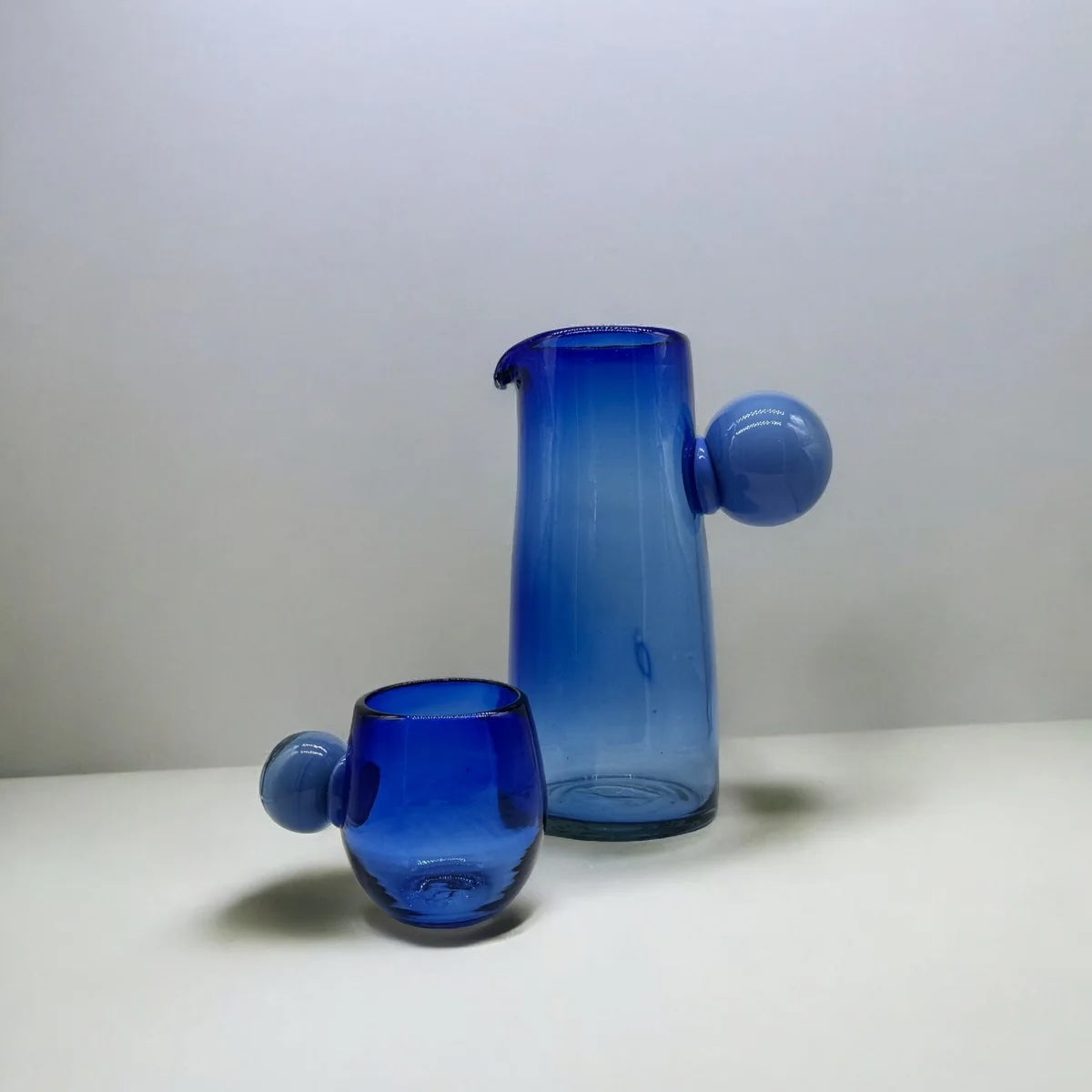 Blue glass carafe and cup on a white surface with a light gray background