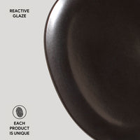 Dark ceramic plate with 'Reactive Glaze' text and 'Each Product is Unique' label on a light gray background
