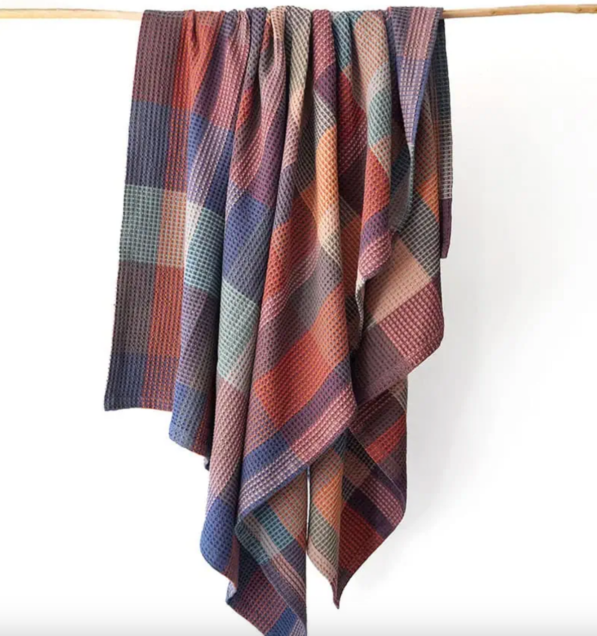Plaid blanket draped over a wooden rod on a white background