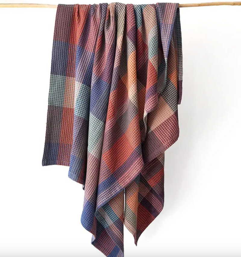 Plaid blanket draped over a wooden rod on a white background