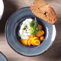 Dish with creamy white sauce, green leaves, and orange elements on a blue ceramic plate with toast.