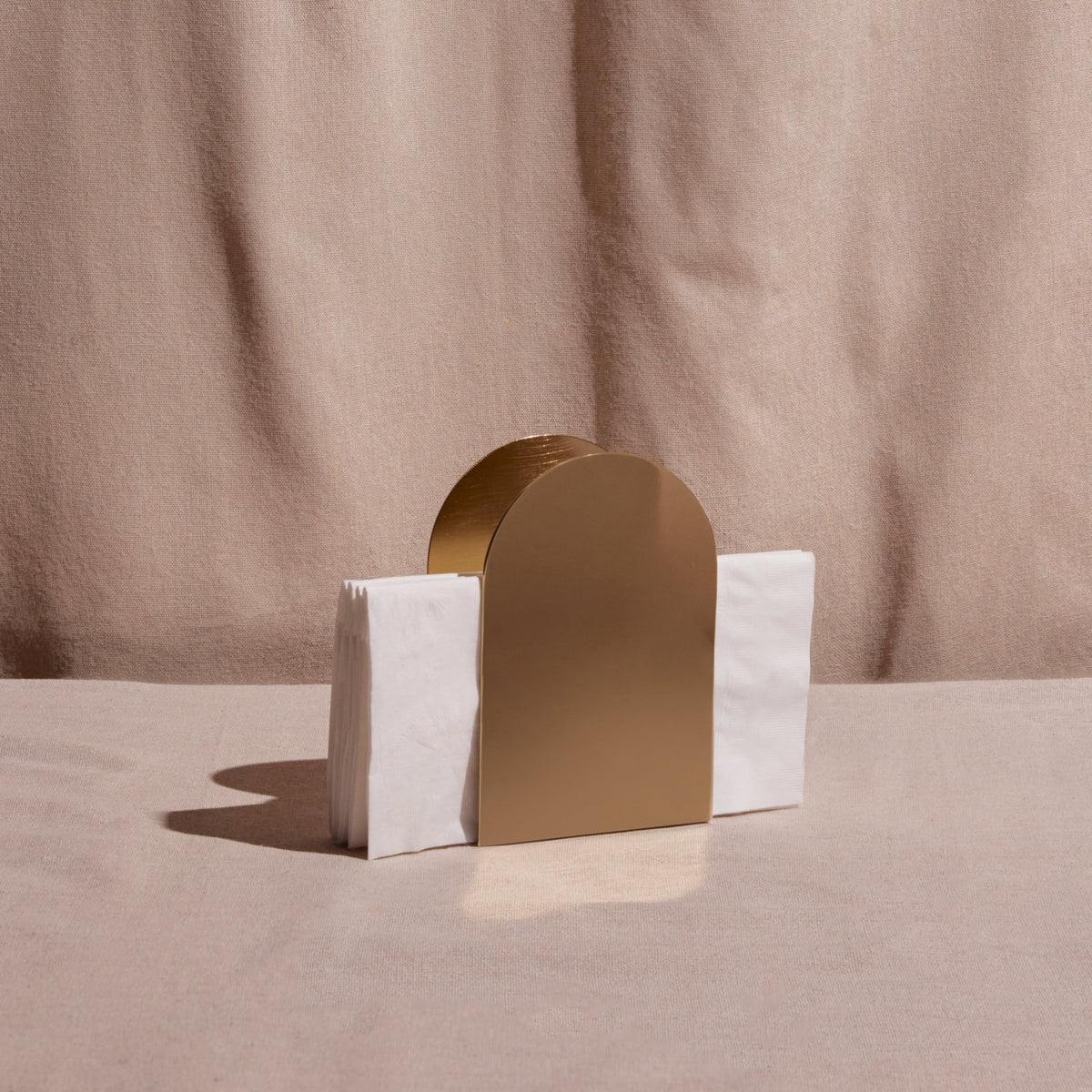 Gold arch-shaped napkin holder on a table against a beige background